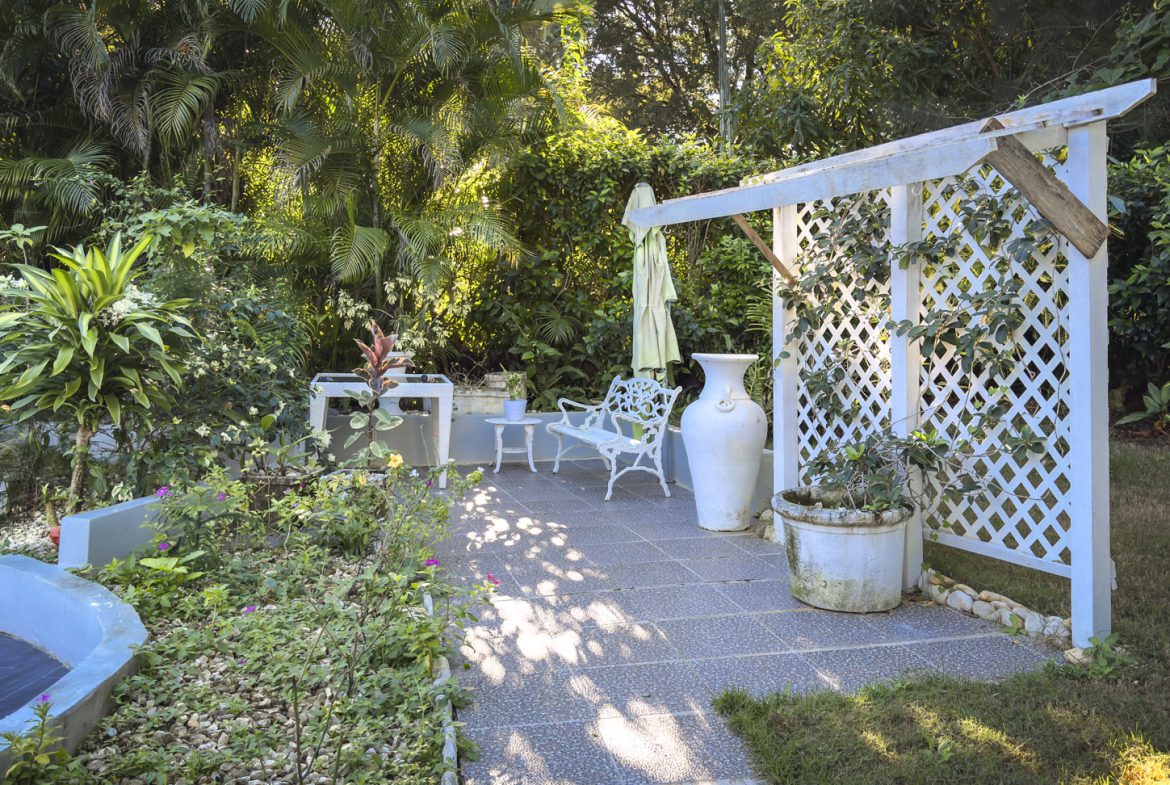 buyDRproperty Colibri villa garden with white pergola, bench, and tropical plants, creating a peaceful oasis. Sosua Real Estate