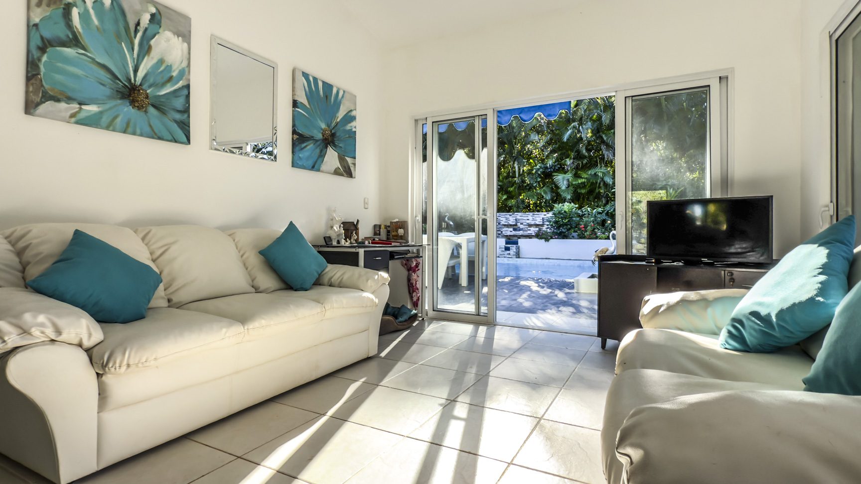 buyDRproperty Villa living room with white sofas, blue accents, and sliding glass doors to a private garden. Sosua Real Estate