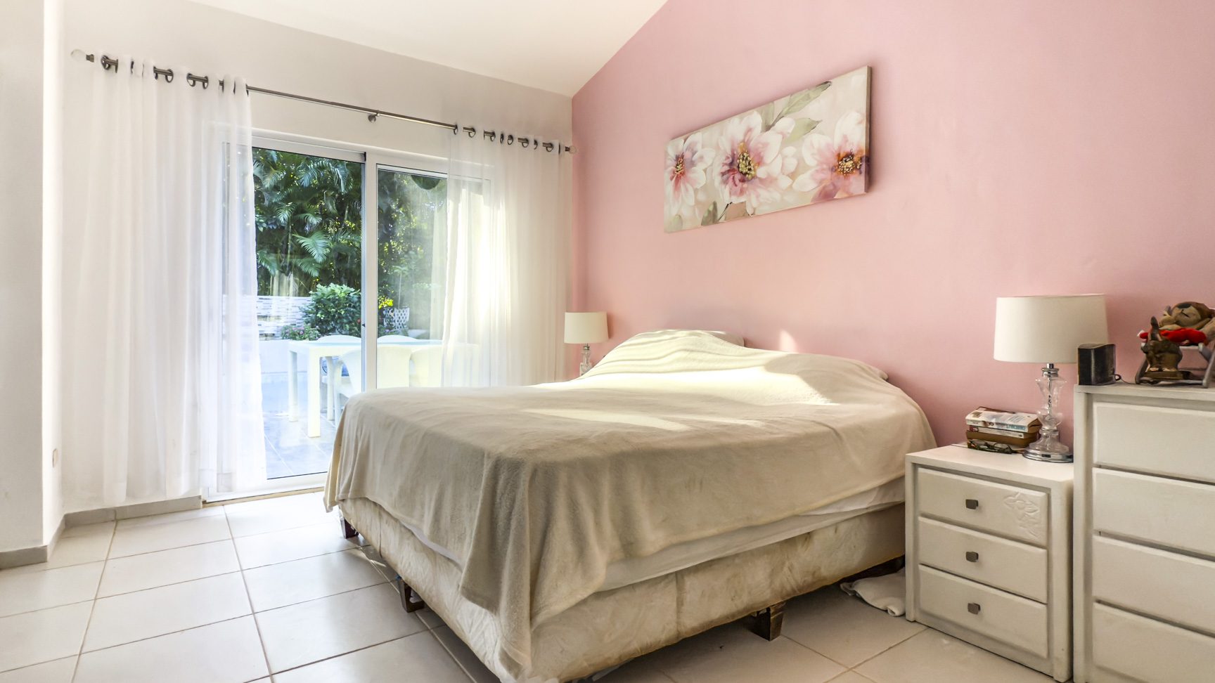 buyDRproperty Bedroom in a villa with pink walls, white tile floor, and sliding glass doors to a garden. Sosua Real Estate