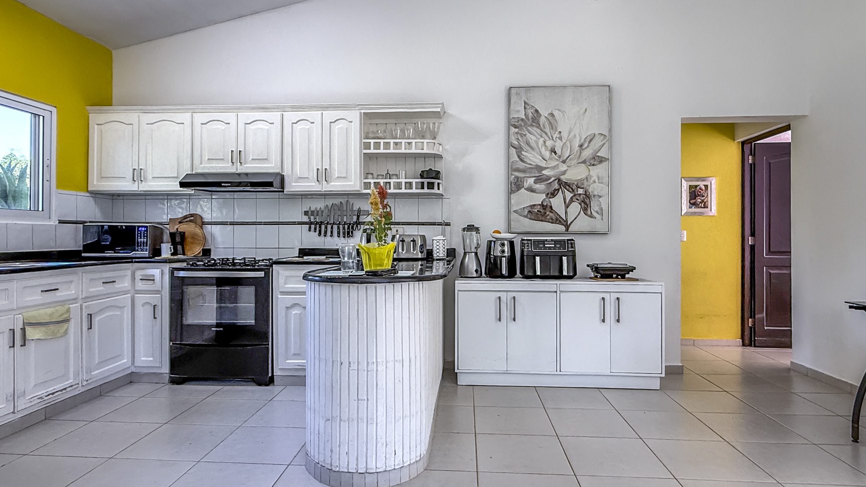 buyDRproperty Bright kitchen in a Colibri villa with white cabinets, black appliances, and yellow accent wall. Sosua Real Estate