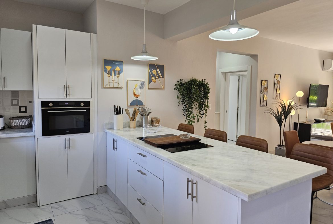 buyDRproperty Bright kitchen with white cabinets, marble island, pendant lights, and modern art. Sosua Real Estate