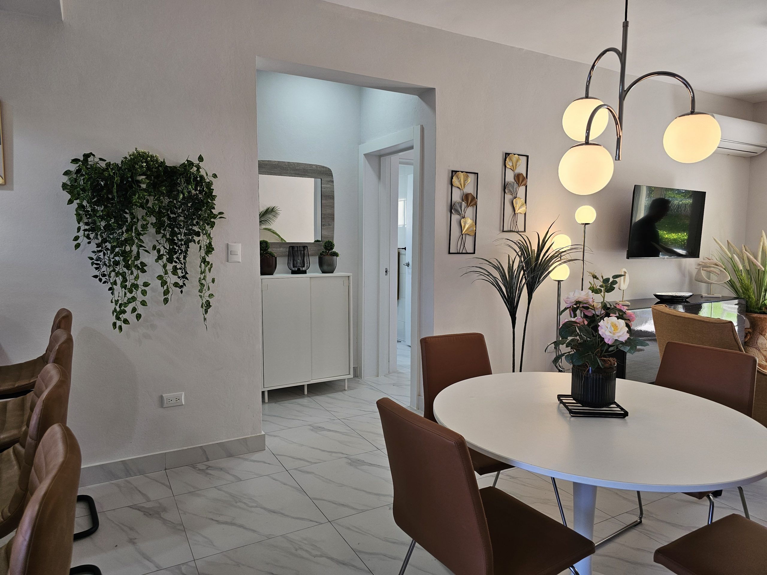buyDRproperty Bright, modern dining area with white table, brown chairs, stylish lighting, and decorative wall accents. Sosua Real Estate