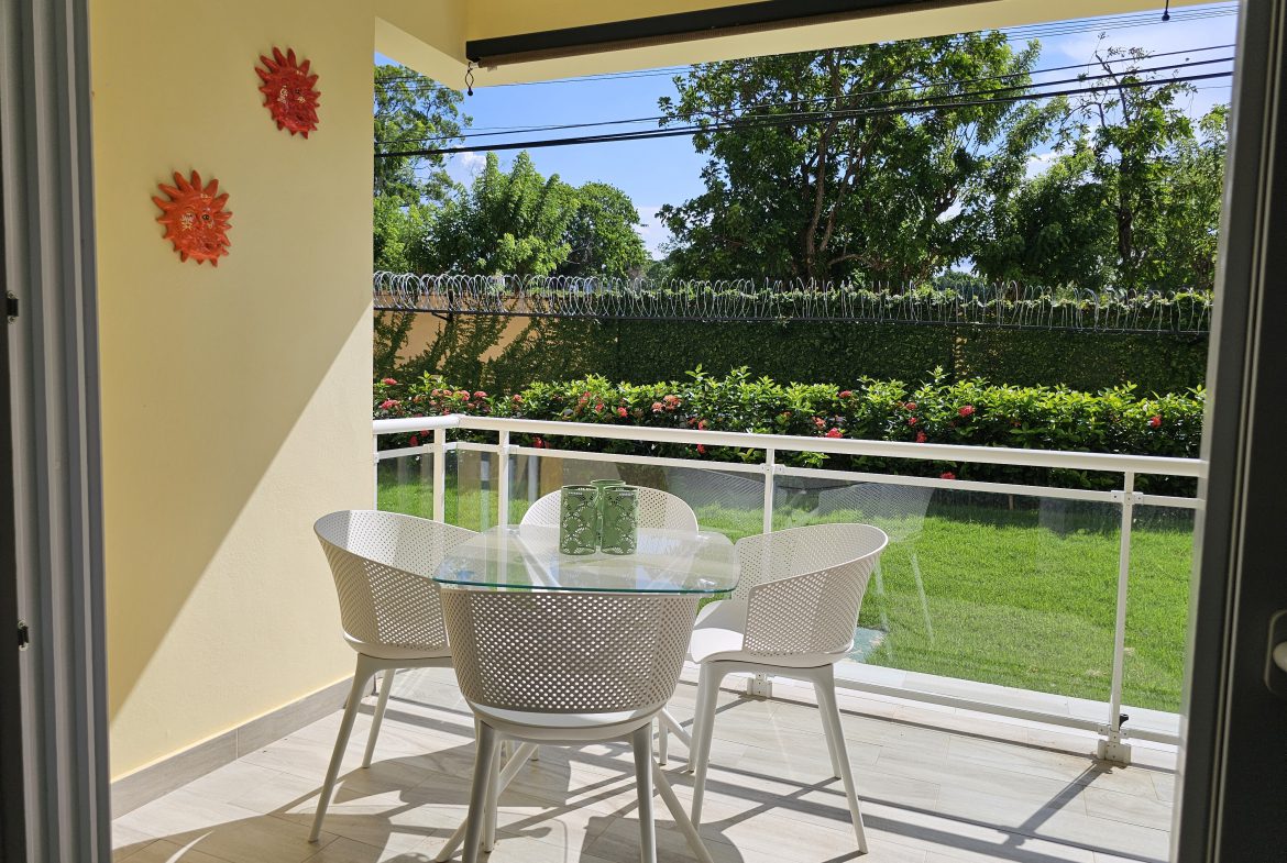 buyDRproperty Outdoor patio with table and chairs overlooking green lawn. Sosua Real Estate