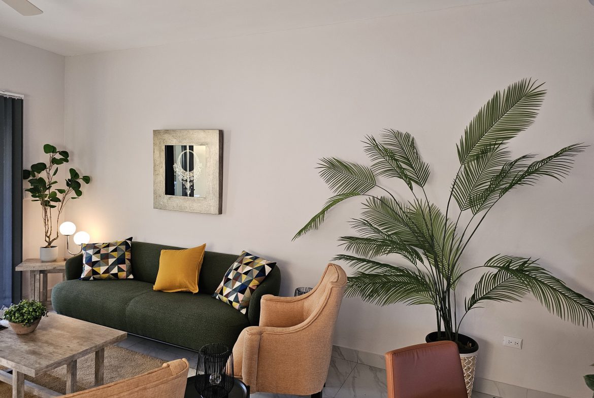 buyDRproperty Stylish living room with green sofa, orange chairs, and a large palm plant. Sosua Real Estate