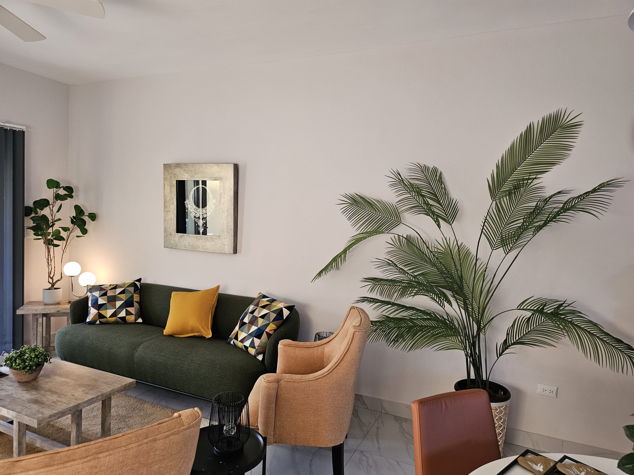 buyDRproperty Stylish living room with green sofa, orange chairs, and a large palm plant. Sosua Real Estate