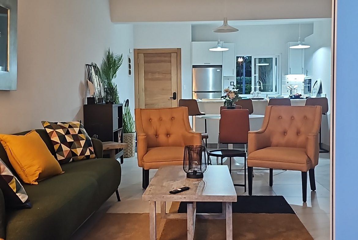 buyDRproperty Modern living room with tan armchairs, green sofa, and white kitchen in the background. Sosua Real Estate