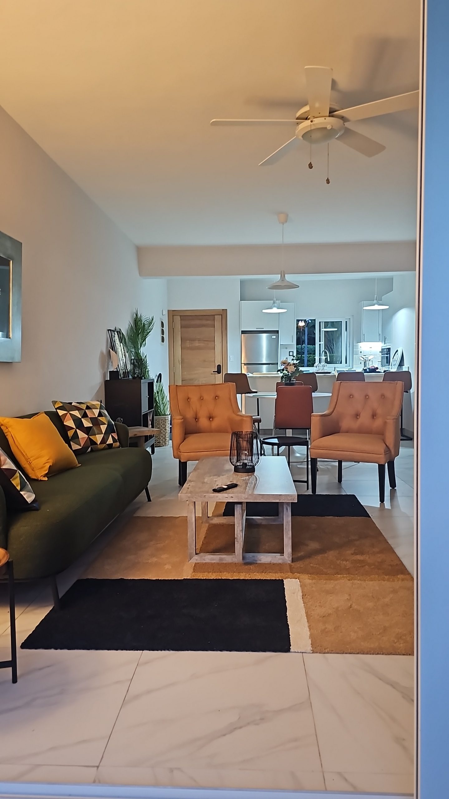 buyDRproperty Modern living room with tan armchairs, green sofa, and white kitchen in the background. Sosua Real Estate