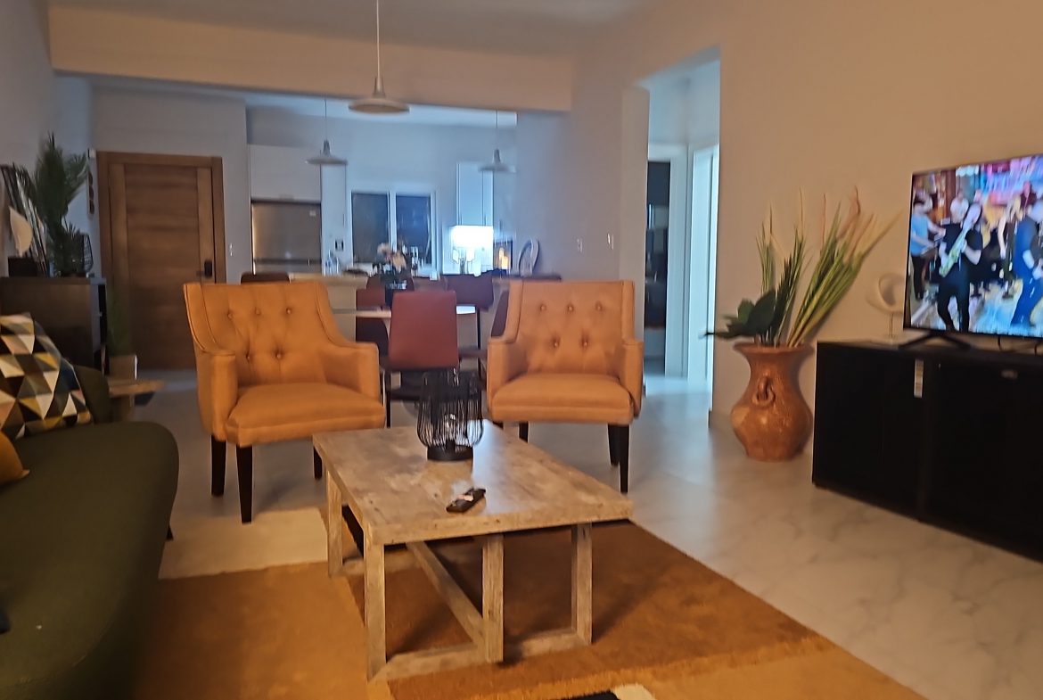 buyDRproperty Cozy living room with tan armchairs, olive green sofa, and TV. Open floor plan home interior. Sosua Real Estate