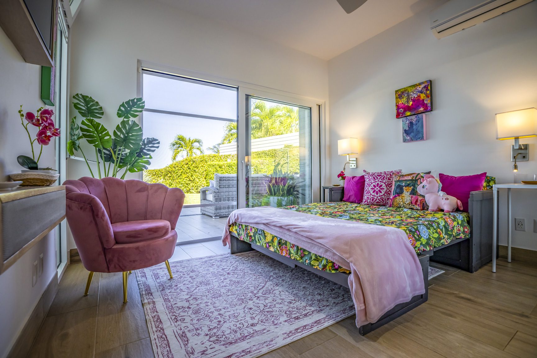 buyDRproperty Bright bedroom with floral bedding, pink chair, and sliding glass doors to a patio. Sosua Real Estate
