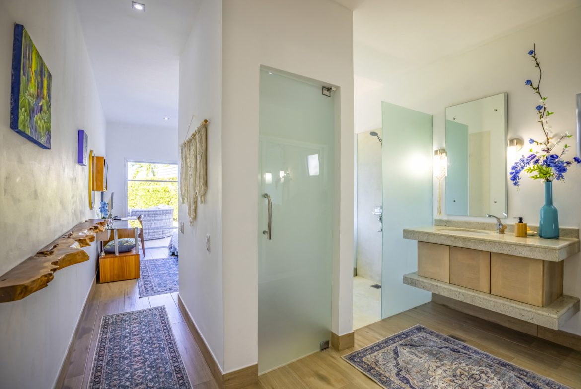 buyDRproperty Modern bathroom with floating vanity, glass shower, and hallway with rustic wood shelf. Sosua Real Estate