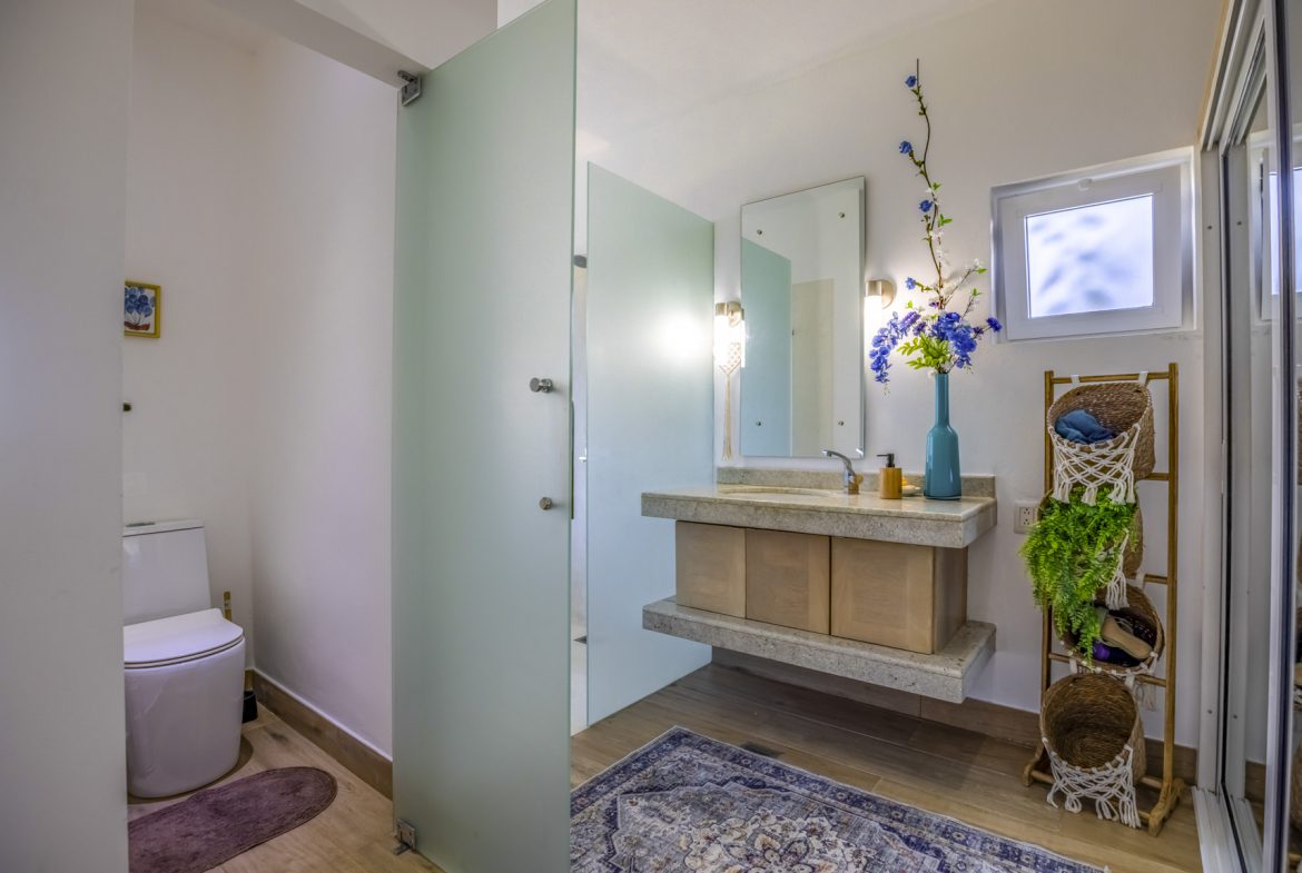 buyDRproperty Modern bathroom with frosted glass door, floating vanity, and blue accents. Sosua Real Estate