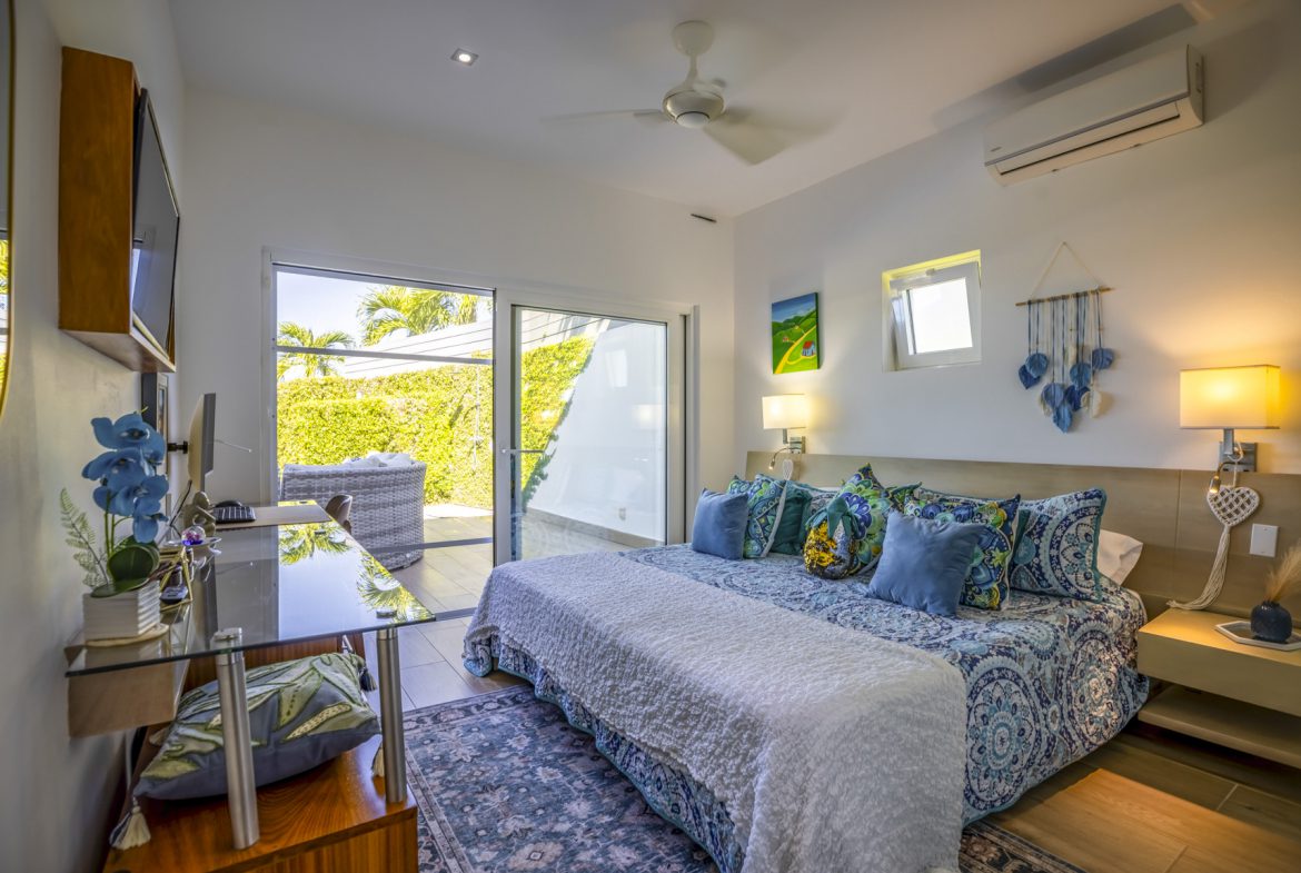 buyDRproperty Bright bedroom with a king-size bed, glass desk, and sliding doors leading to a sunny patio. Sosua Real Estate