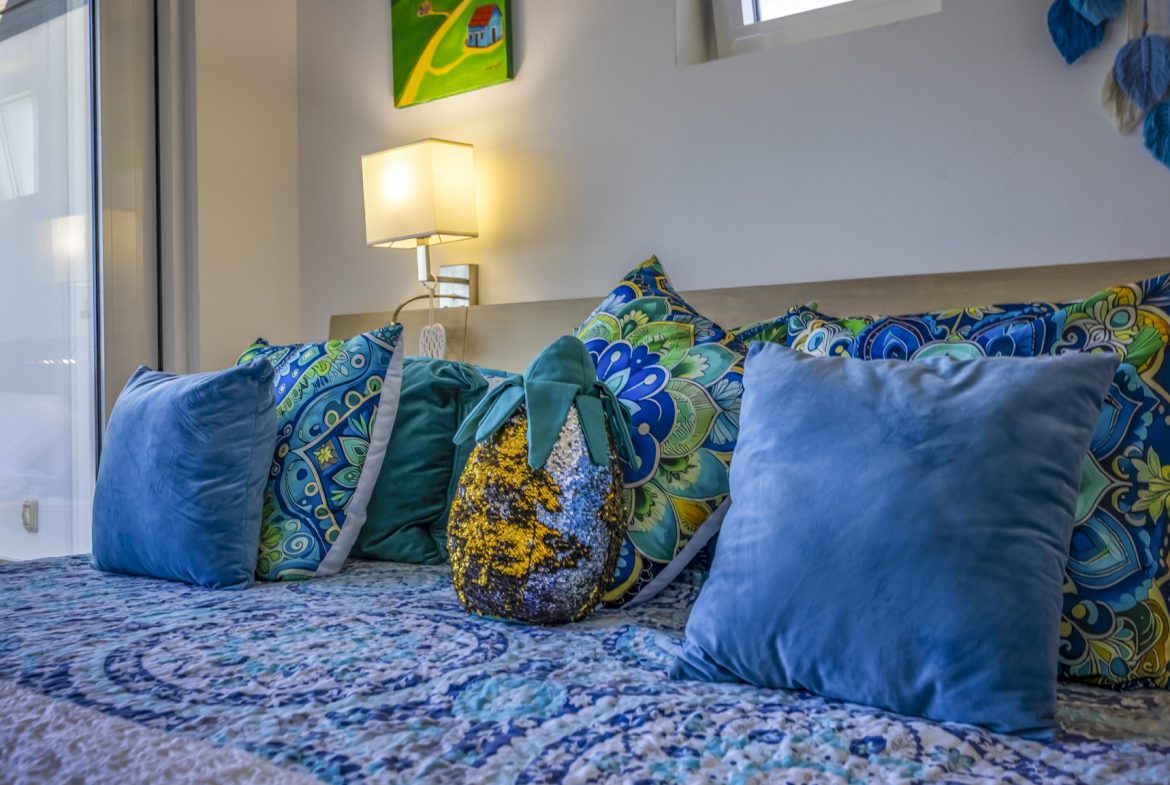 buyDRproperty Cozy bed with blue and turquoise patterned bedding and decorative pillows. Sosua Real Estate