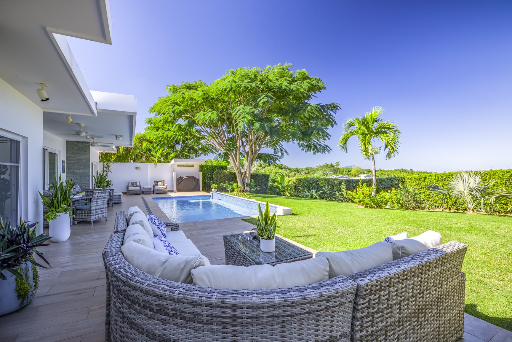 buyDRproperty Luxury backyard with pool, modern white house, lush green lawn, and outdoor wicker furniture. Sosua Real Estate