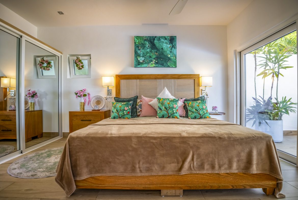 buyDRproperty Bedroom with wooden bed, green and pink pillows, abstract art, and sliding glass doors to a patio. Sosua Real Estate