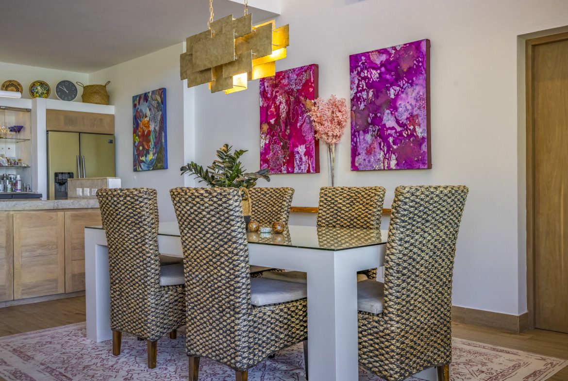 buyDRproperty Dining room with woven chairs, glass table, and vibrant pink artwork. Sosua Real Estate