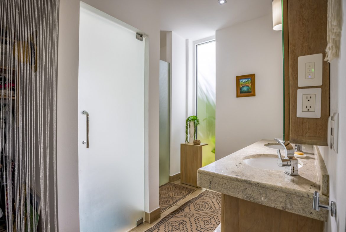buyDRproperty Modern bathroom with frosted glass shower door, stone countertop, and geometric rug. Sosua Real Estate