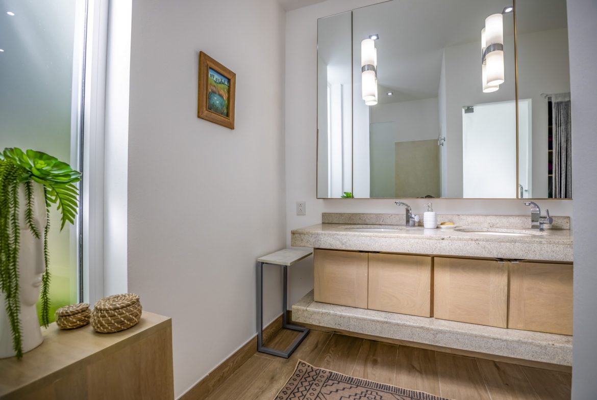 buyDRproperty Modern bathroom with double vanity, light wood cabinets, stone countertop, and decorative accents. Sosua Real Estate
