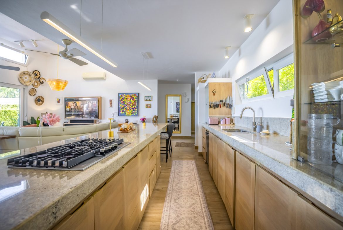 buyDRproperty Bright, modern kitchen with island cooktop, light wood cabinets, and open living space. Sosua Real Estate