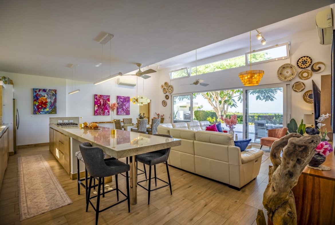 buyDRproperty Bright, open-concept living room with kitchen island, beige sofa, and patio view. Sosua Real Estate