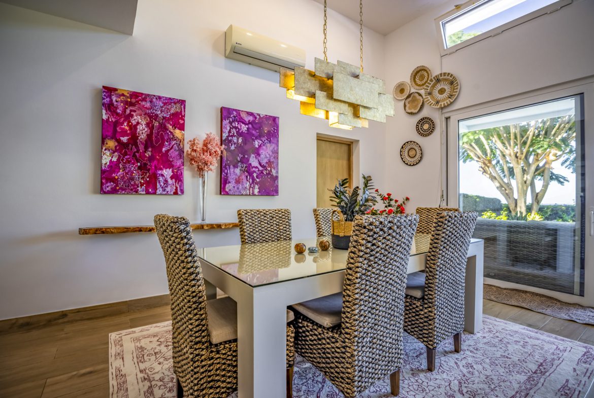 buyDRproperty Bright dining room featuring a white table, wicker chairs, and vibrant pink abstract art on the wall. Sosua Real Estate