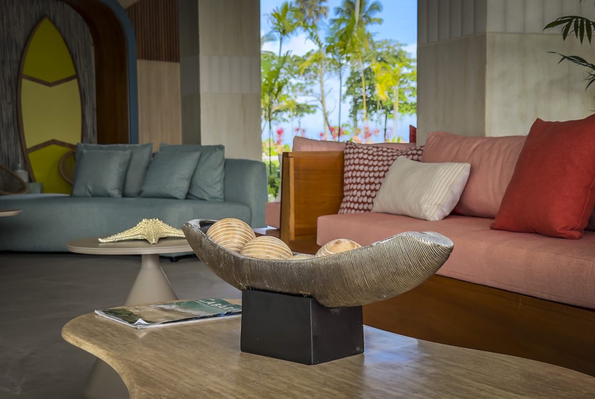 buyDRproperty Coastal-themed hotel lobby with blue and pink sofas, surfboard decor, and tropical view. Sosua Real Estate