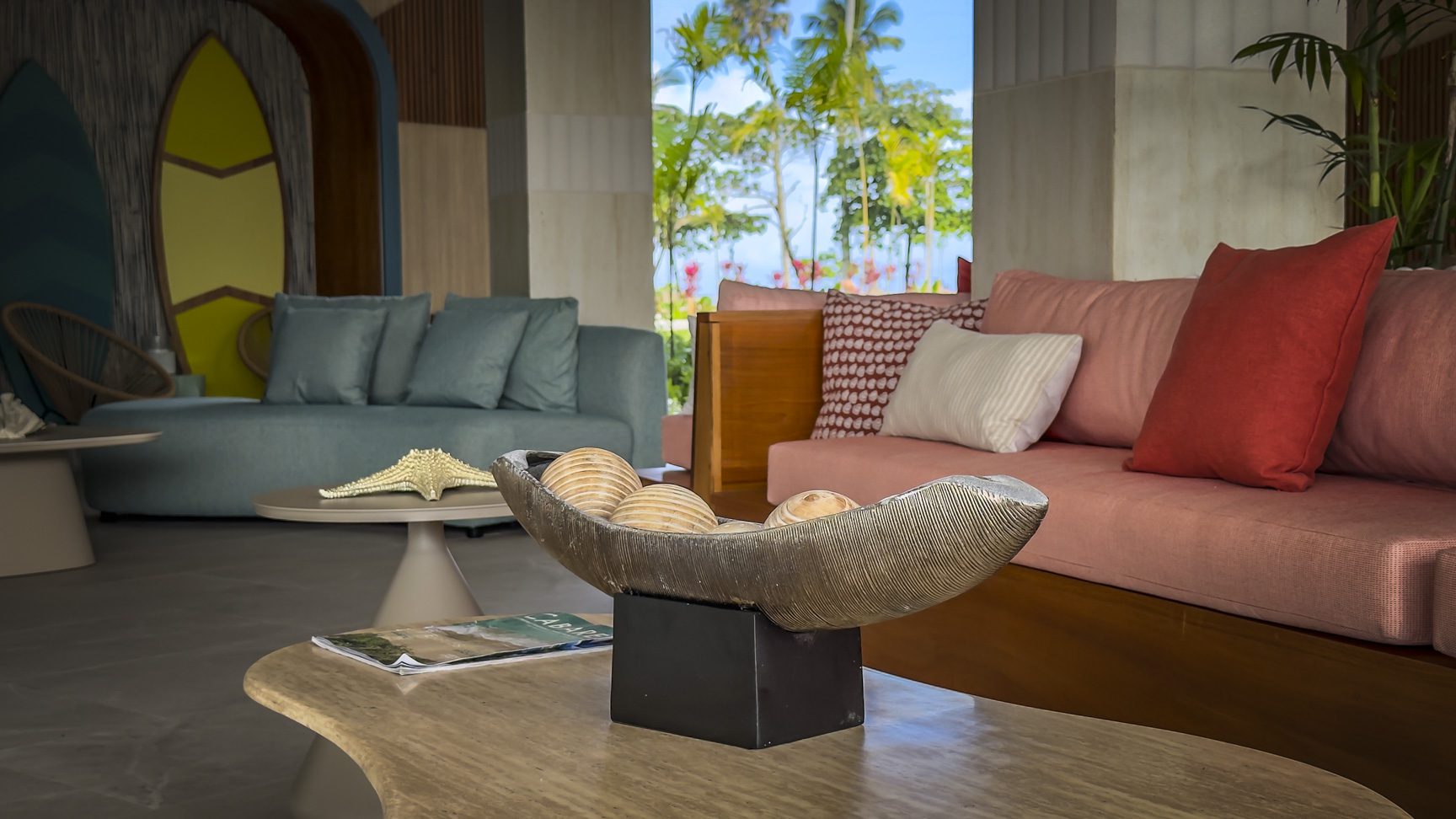 buyDRproperty Coastal-themed hotel lobby with blue and pink sofas, surfboard decor, and tropical view. Sosua Real Estate