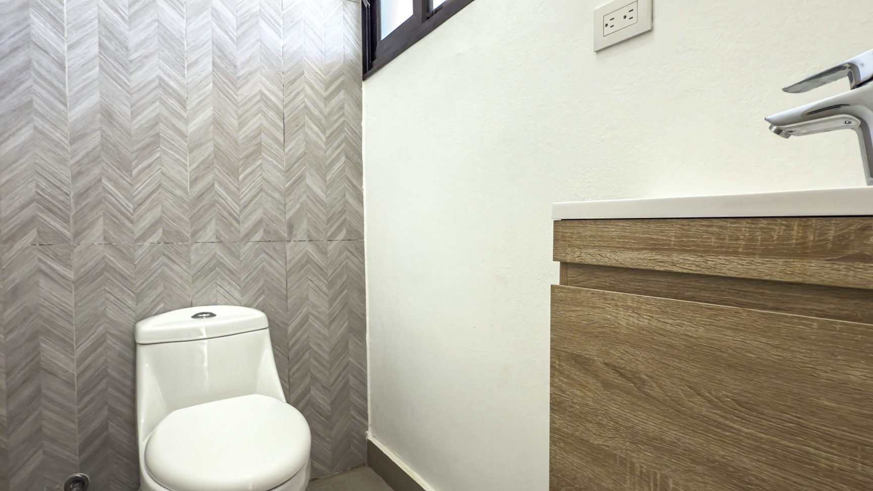 buyDRproperty Modern bathroom with white toilet, wood vanity, chevron tile wall, and electrical outlet. Sosua Real Estate