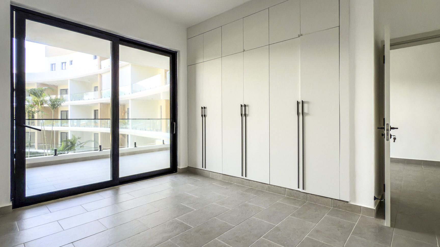 buyDRproperty Bright room with sliding glass door, built-in white wardrobe, and gray tile floor. Sosua Real Estate