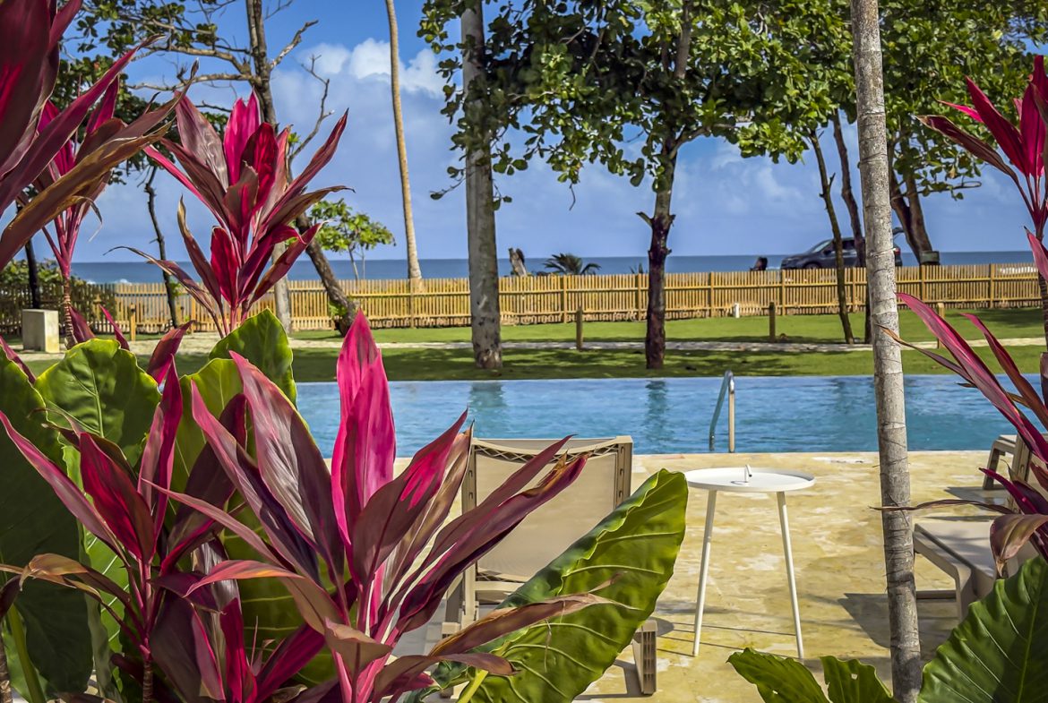 buyDRproperty Tropical resort pool with lounge chairs, vibrant red plants, and a view of the ocean. Sosua Real Estate