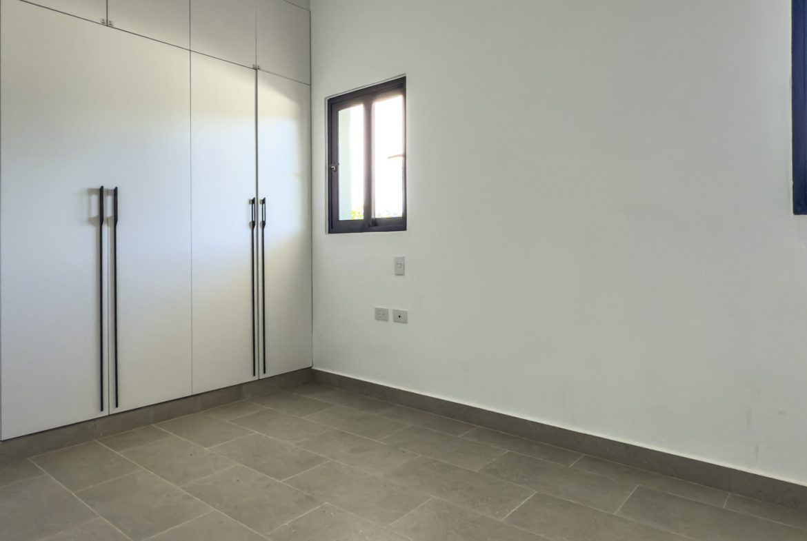 buyDRproperty Modern bedroom with built-in white wardrobe, gray tile floor, and black framed windows. Sosua Real Estate