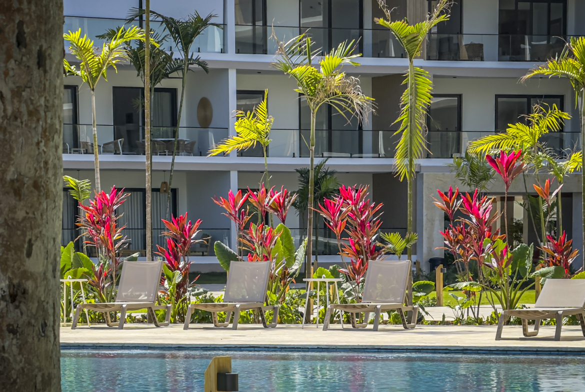 buyDRproperty Poolside lounge chairs at a modern resort with tropical plants and palm trees. Sosua Real Estate