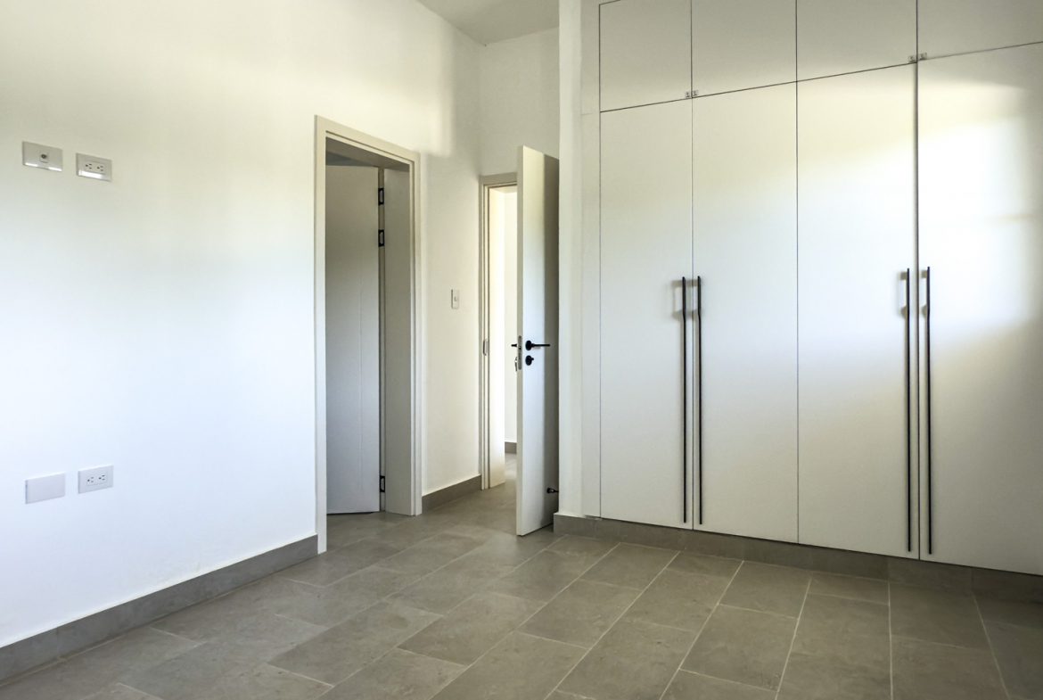 buyDRproperty Bright, modern bedroom with built-in white wardrobes and neutral tile flooring. Sosua Real Estate