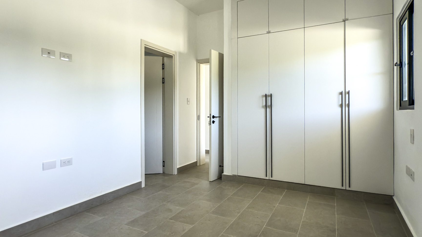 buyDRproperty Bright, modern bedroom with built-in white wardrobes and neutral tile flooring. Sosua Real Estate