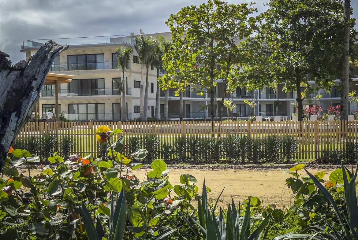 buyDRproperty Modern beachfront condo behind a wooden fence with tropical plants in the foreground. Sosua Real Estate