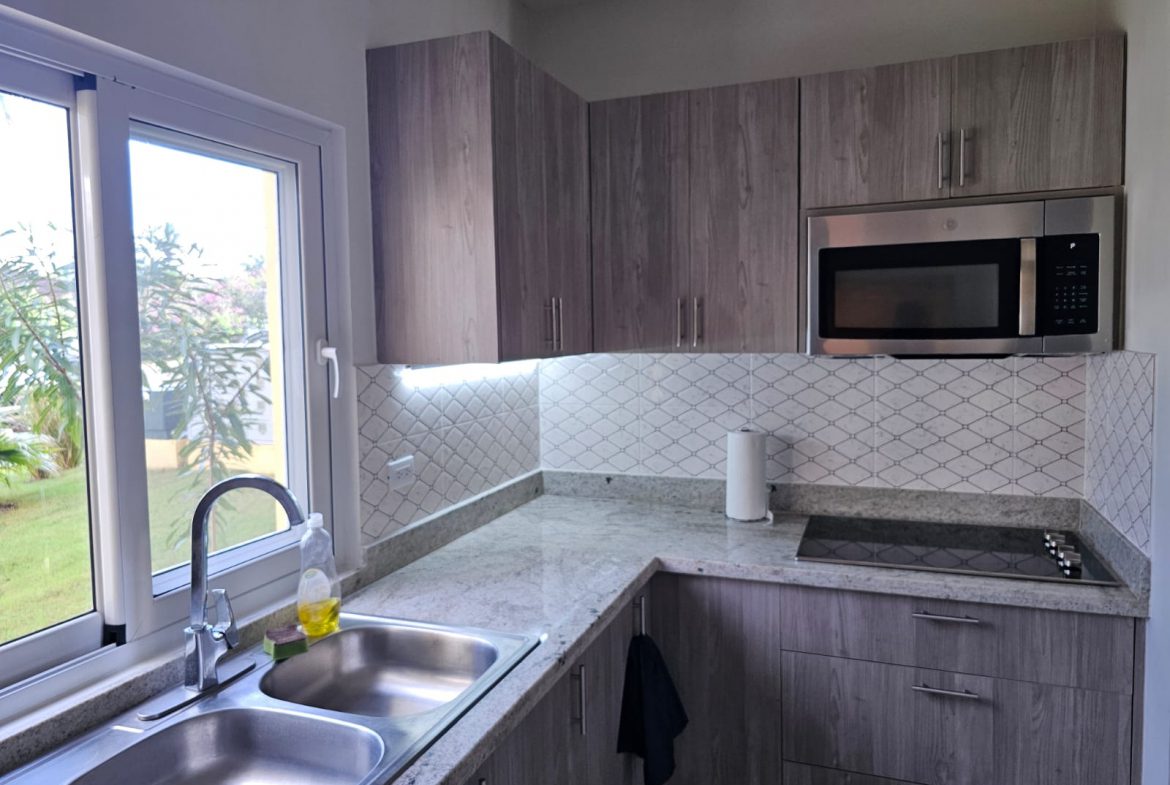 buyDRproperty Modern kitchen with stainless steel appliances, gray cabinets, granite countertops, and a large window. Sosua Real Estate