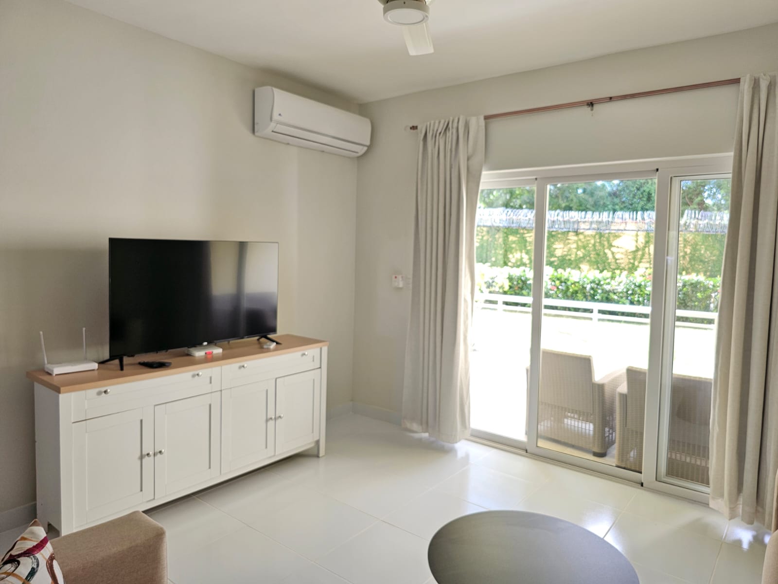 buyDRproperty Bright living room with white TV cabinet, air conditioner, and sliding glass doors to a patio. Sosua Real Estate