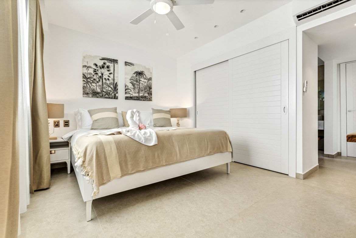 buyDRproperty Bright bedroom with white bed, sliding closet, tropical art, and towel swans. Sosua Real Estate