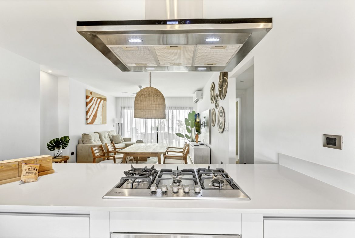 buyDRproperty Modern kitchen with stainless steel stove and hood, leading to open-plan living and dining area. Sosua Real Estate