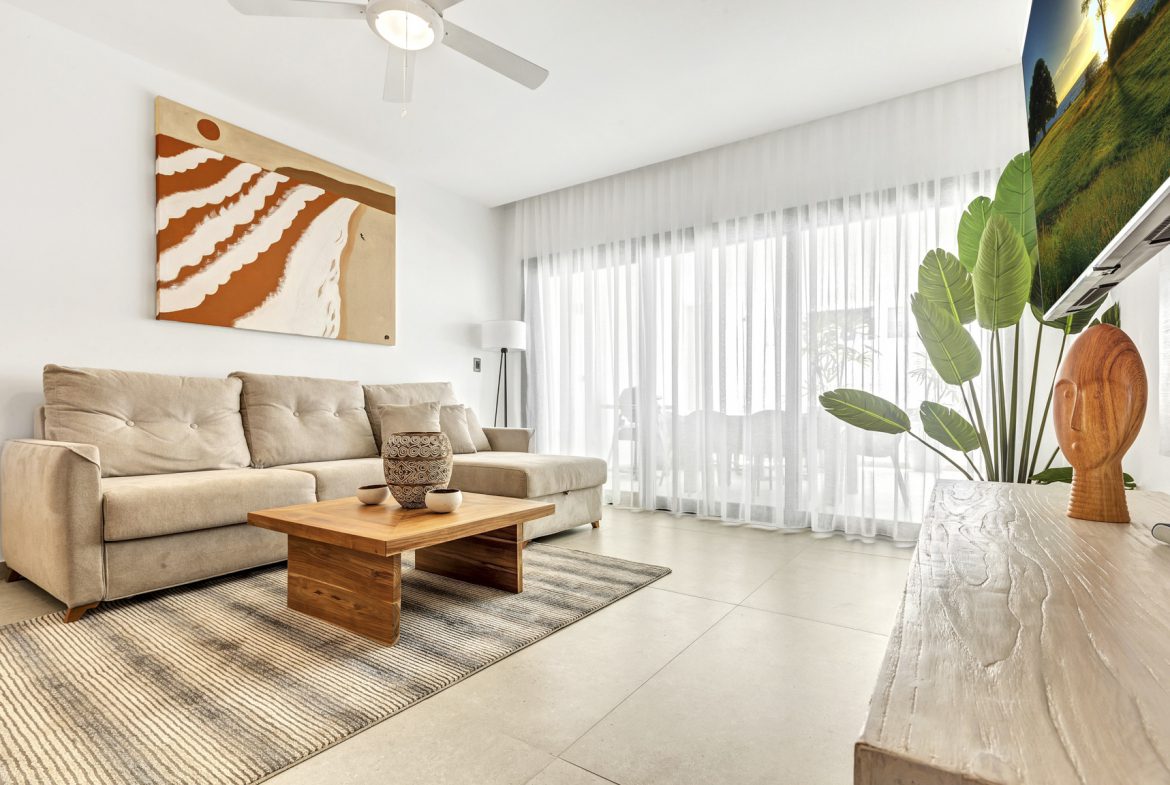 buyDRproperty Bright living room with beige sofa, modern art, and sheer curtains. Sosua Real Estate