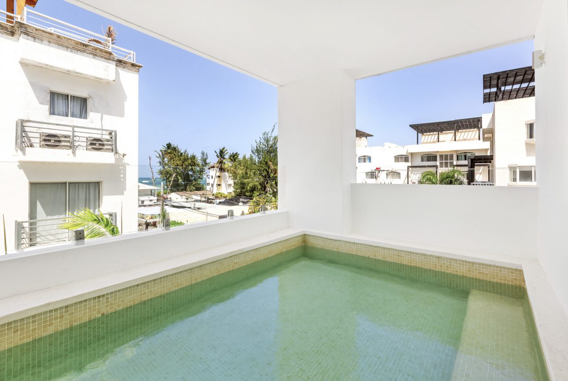 buyDRproperty Private rooftop pool with turquoise water overlooking buildings and palm trees on a sunny day. Sosua Real Estate