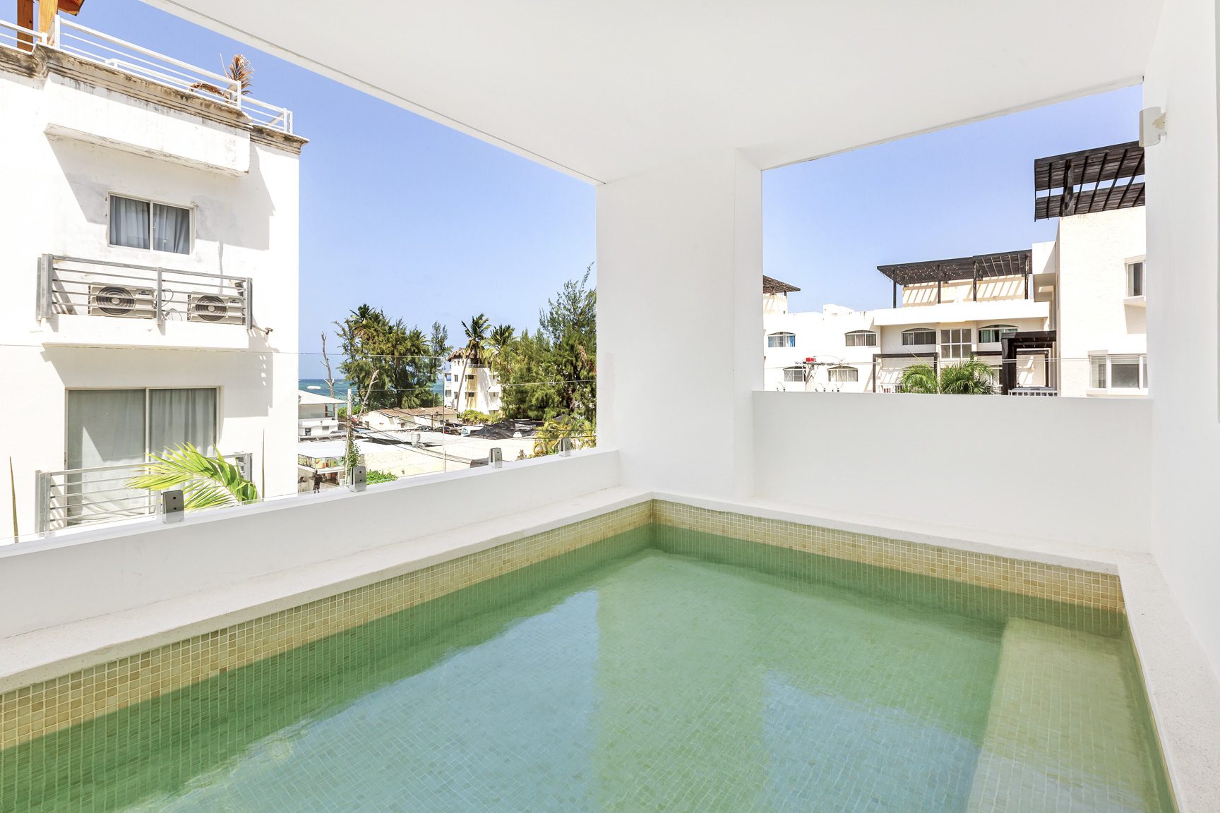 buyDRproperty Private rooftop pool with turquoise water overlooking buildings and palm trees on a sunny day. Sosua Real Estate