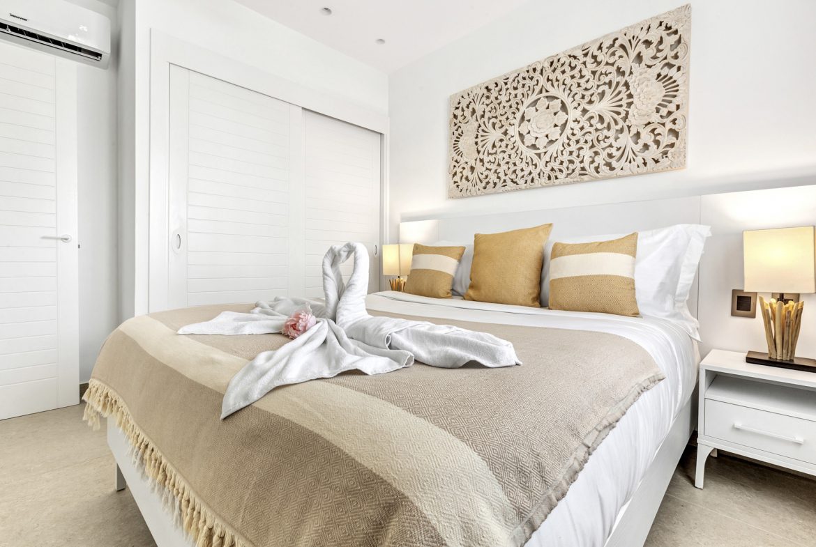 buyDRproperty Luxurious bedroom with swan towel art, gold cushions, and carved wooden headboard. Sosua Real Estate