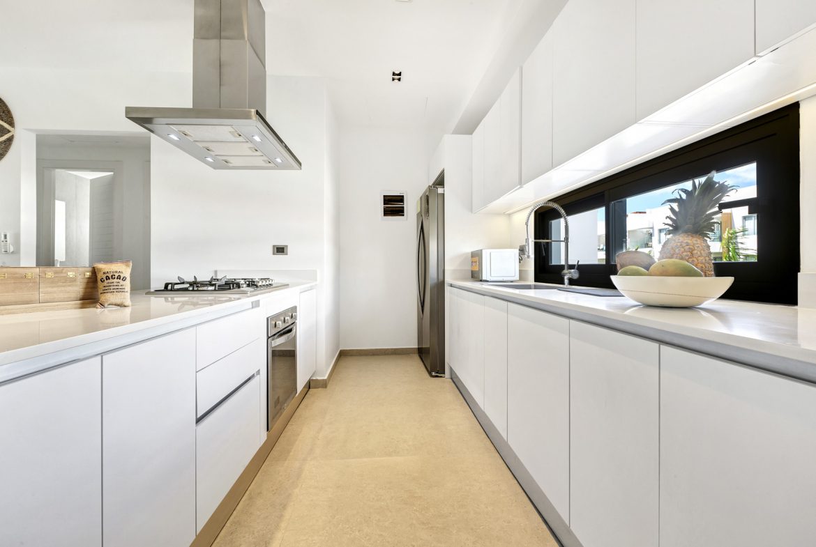 buyDRproperty Modern white kitchen with stainless steel appliances and a large window showing tropical foliage. Sosua Real Estate