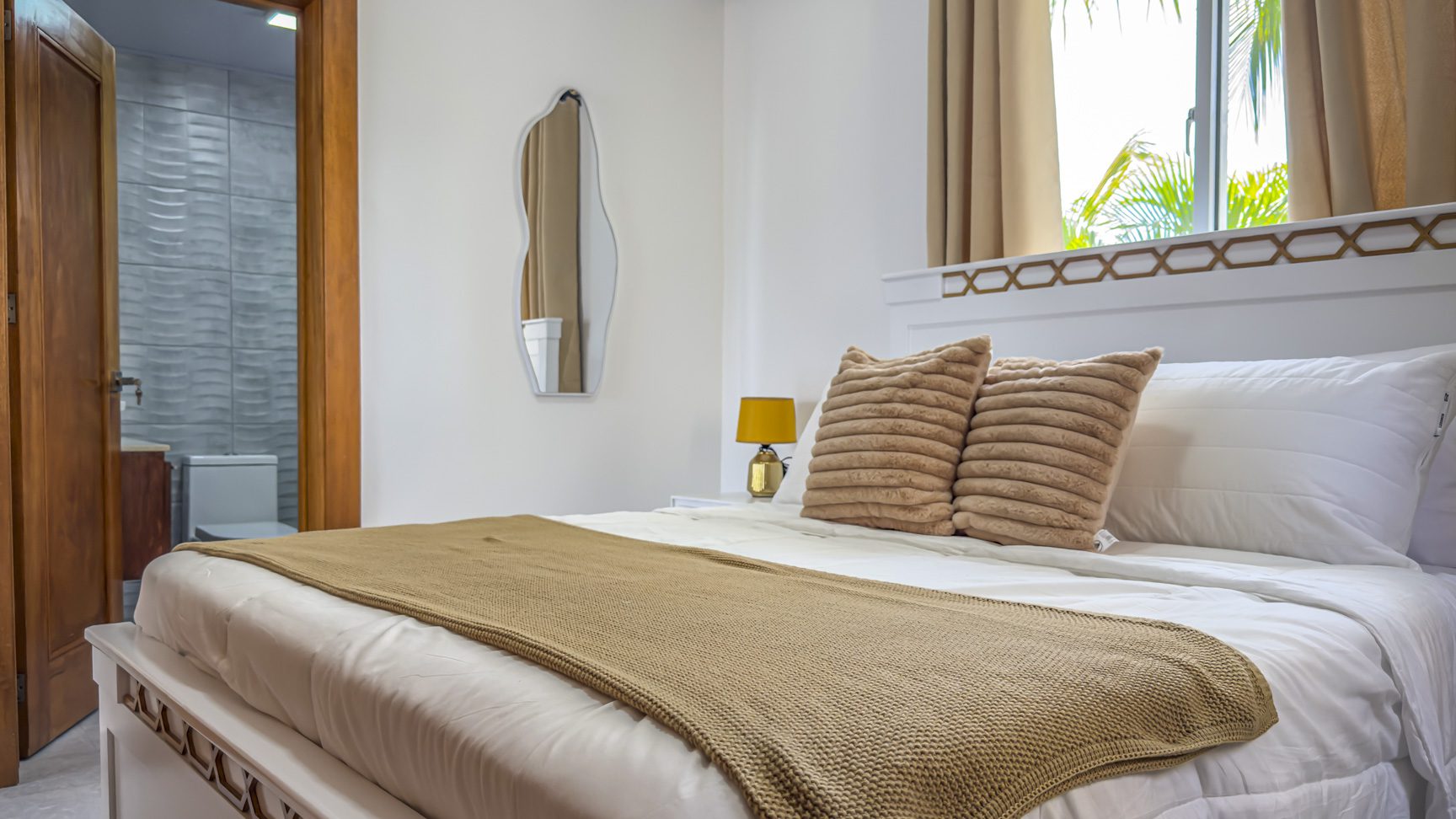 Bright bedroom with white bedding, neutral accents, and bathroom access.