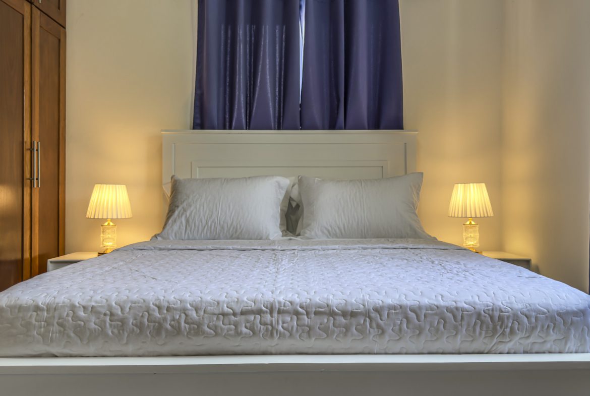 Cozy small bedroom with white bed and warm lighting.