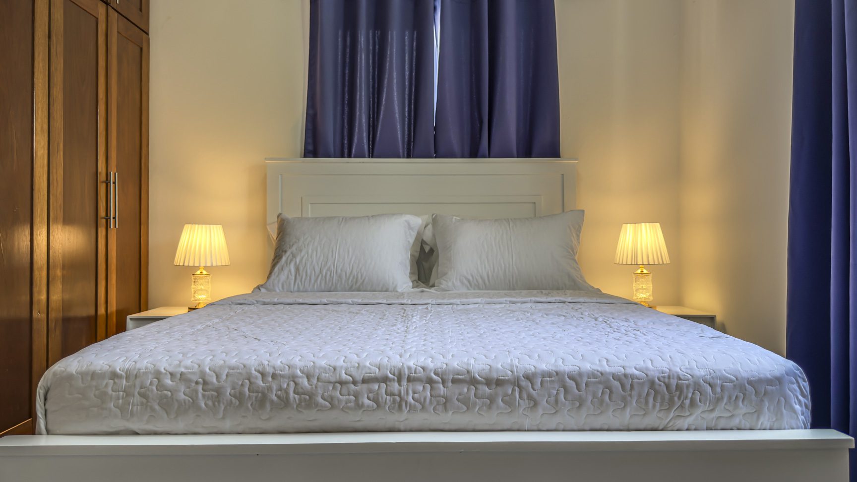 Cozy small bedroom with white bed and warm lighting.