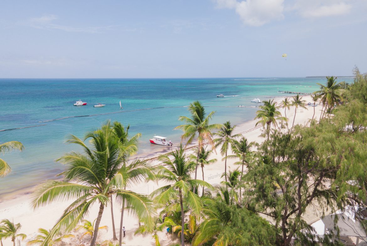buyDRproperty Tropical beach scene with palm trees, white sand, turquoise water, and boats under a sunny sky. Sosua Real Estate