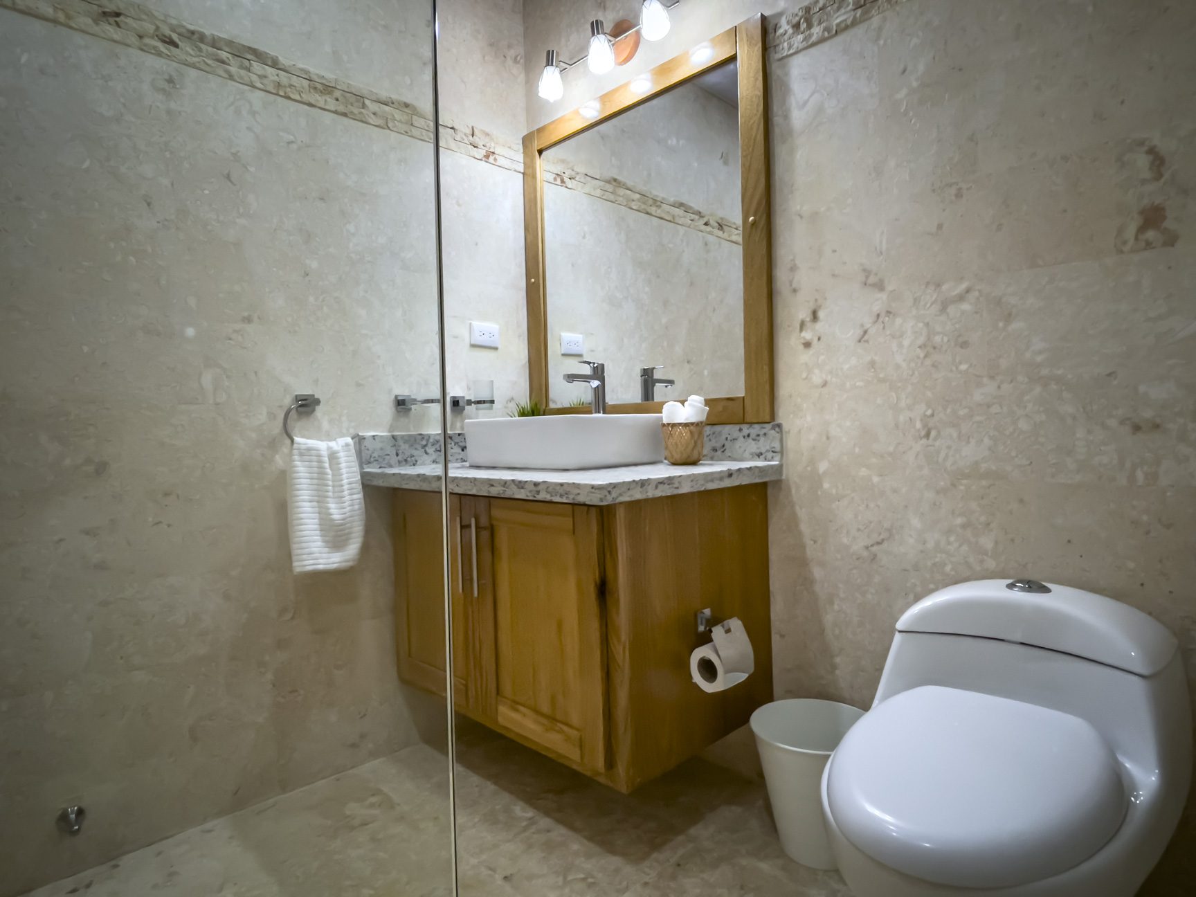 buyDRproperty Bathroom with modern sink, toilet, granite countertop, wood cabinet, and neutral tile walls. Sosua Real Estate