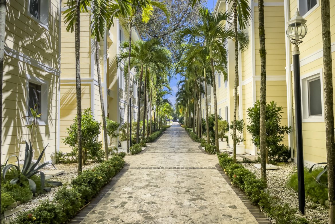 buyDRproperty Tropical walkway lined with palm trees and yellow buildings under a blue sky. Sosua Real Estate